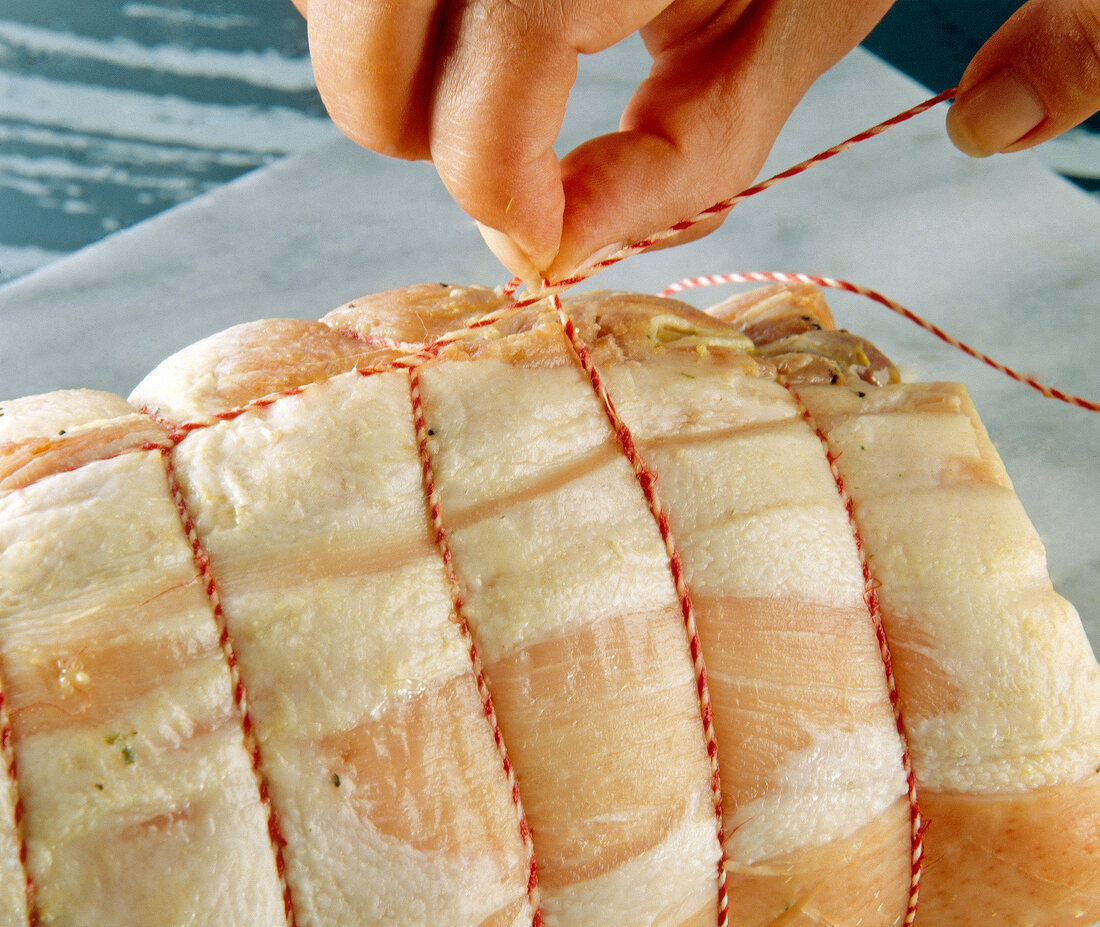 Close-up of woman's hands making node at the end of the wrapped roast