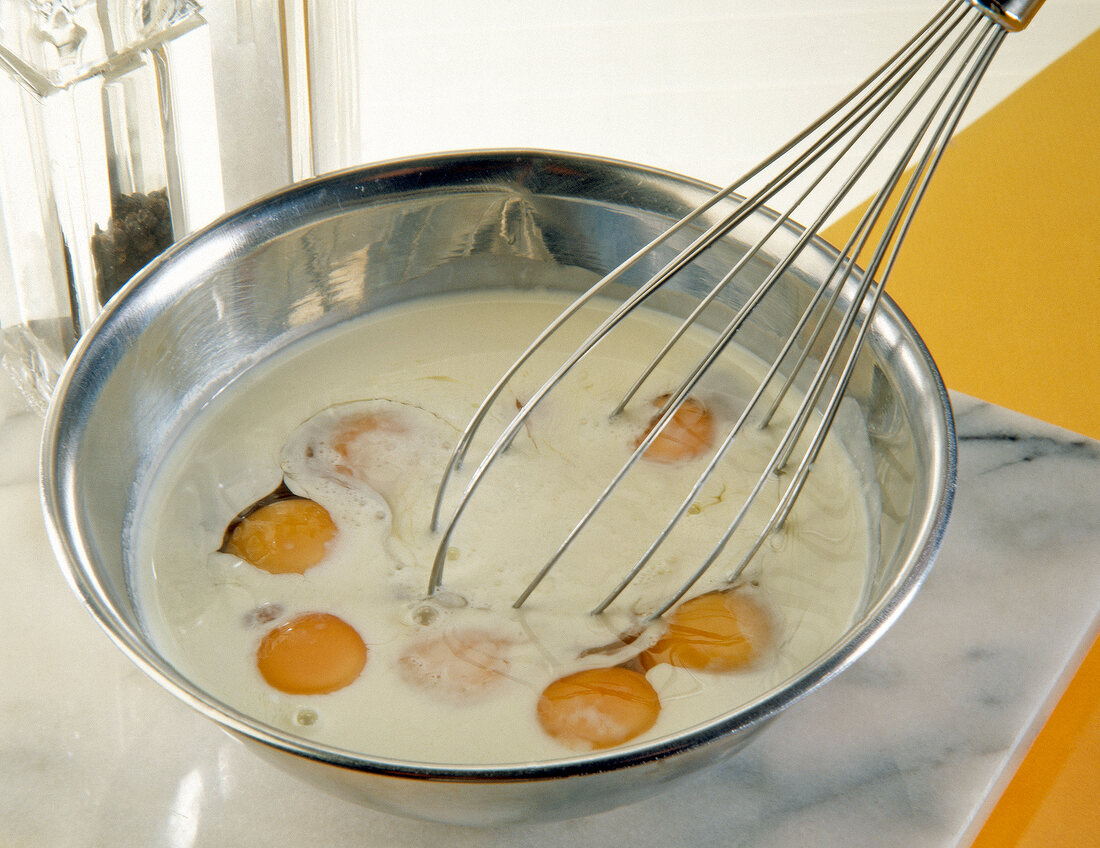 Close-up of eggs and cream being beaten with a whisk in steel bowl