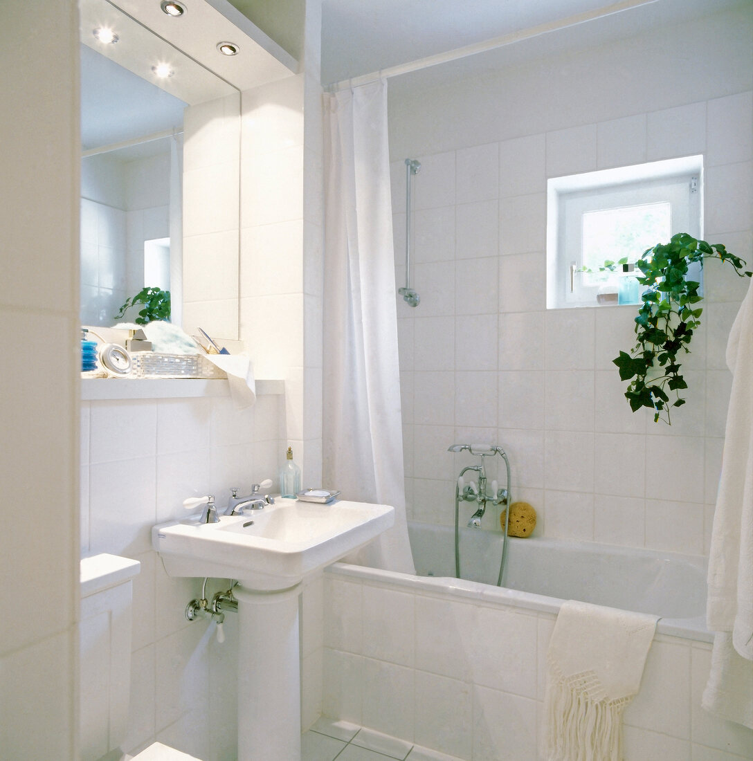 Interior of white tiled bathroom with sink, mirror and bathtub