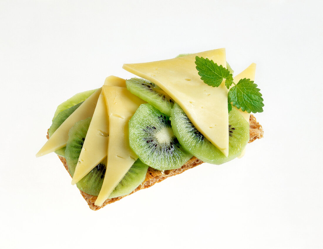 Slice of crisp bread with cheese, kiwi and lemon balm