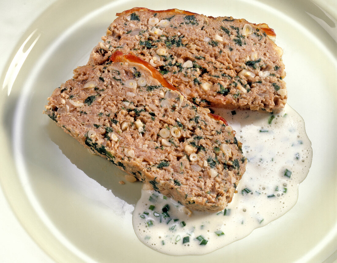 Two pieces of meatloaf with spinach and pine nuts and garlic sauce