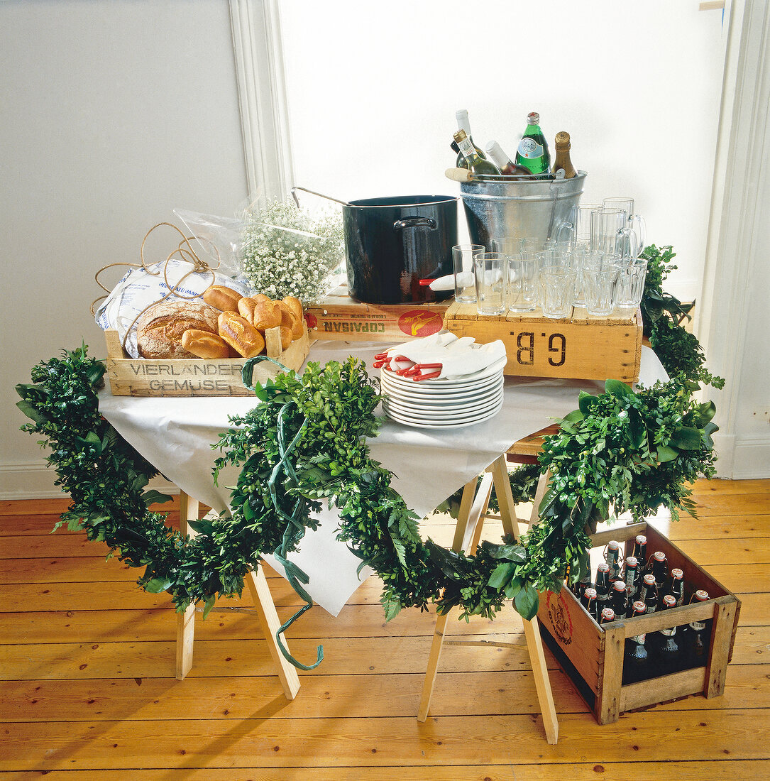 Buffet table with bread, bucket with drinks, flower garland and glasses