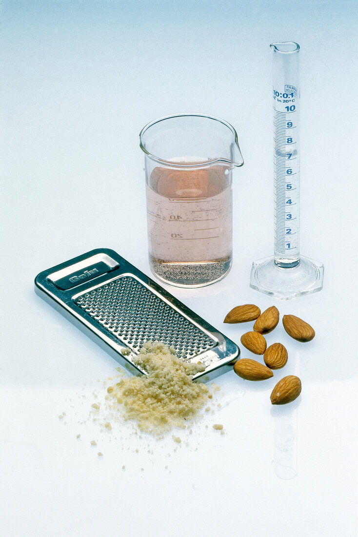 Almonds, steel grater and rose water in measuring glass and tube on white background