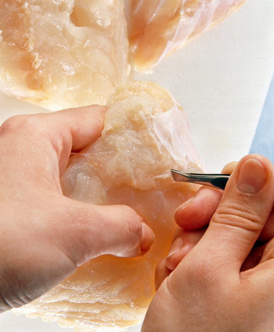 Close-up of woman's hand plucking bones with tweezers from cod fillets