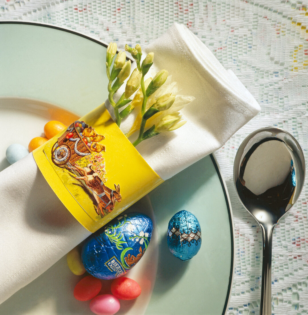Napkin folded with flowers in yellow napkin ring, spoon and Easter eggs on plate