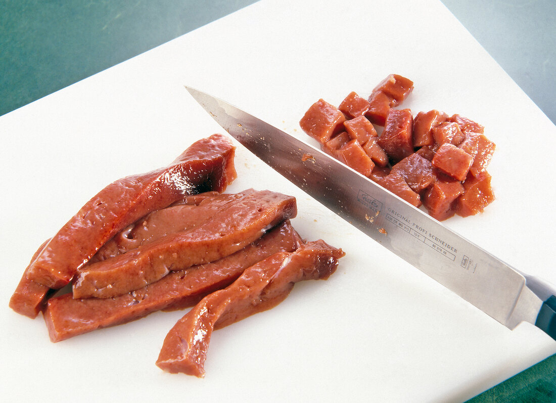 Breast of veal cut into pieces with knife on white chopping board