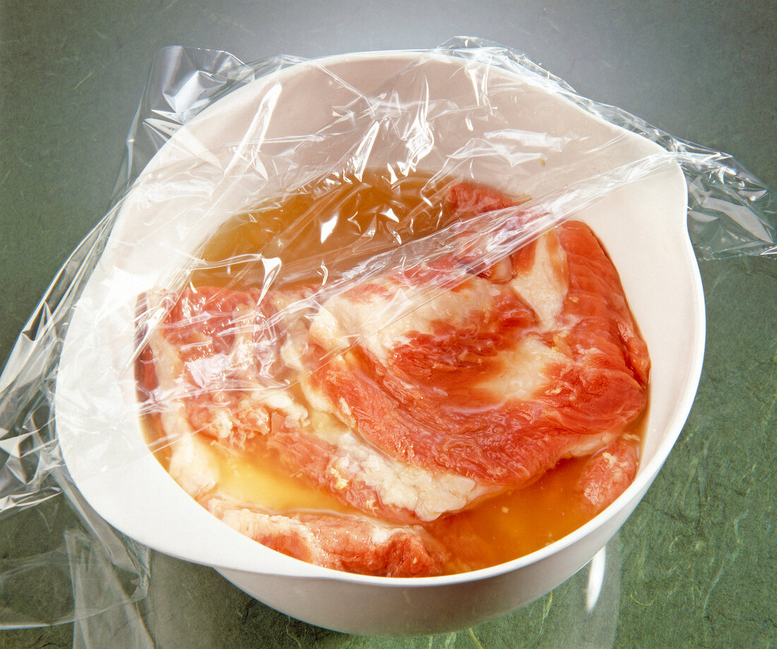 Veal breast marinated in bowl covered with plastic from top