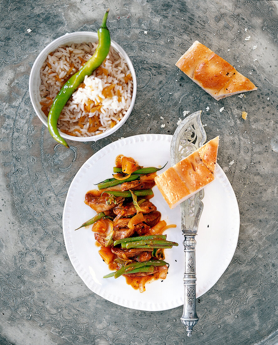 Roasted lamb on plate and pilaf in bowl, overhead view