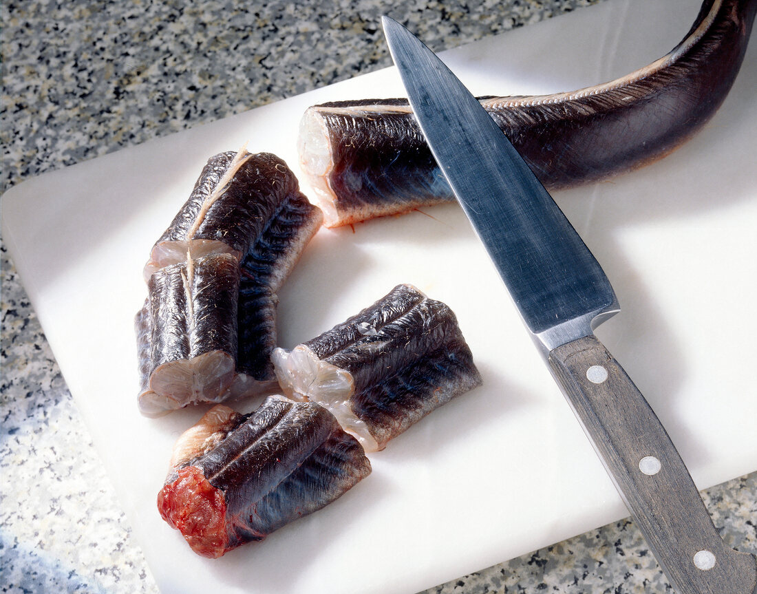 Raw eel cut in pieces on cutting board with knife