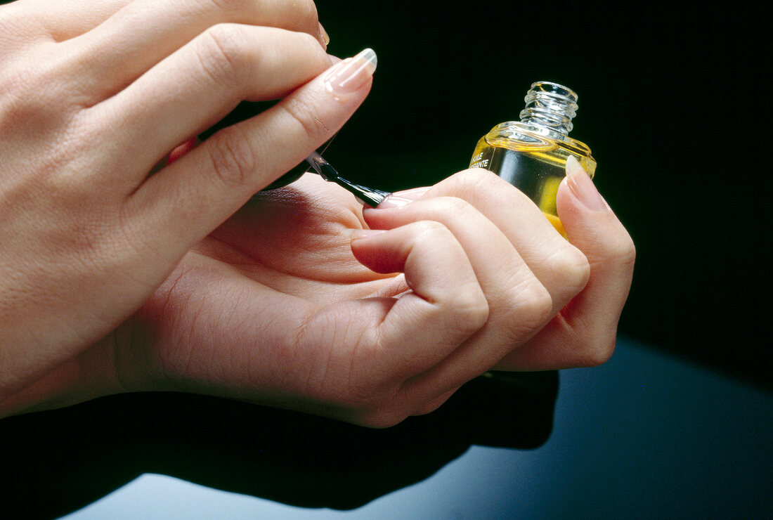 Close-up of woman's hand applying nail oil to finger nails