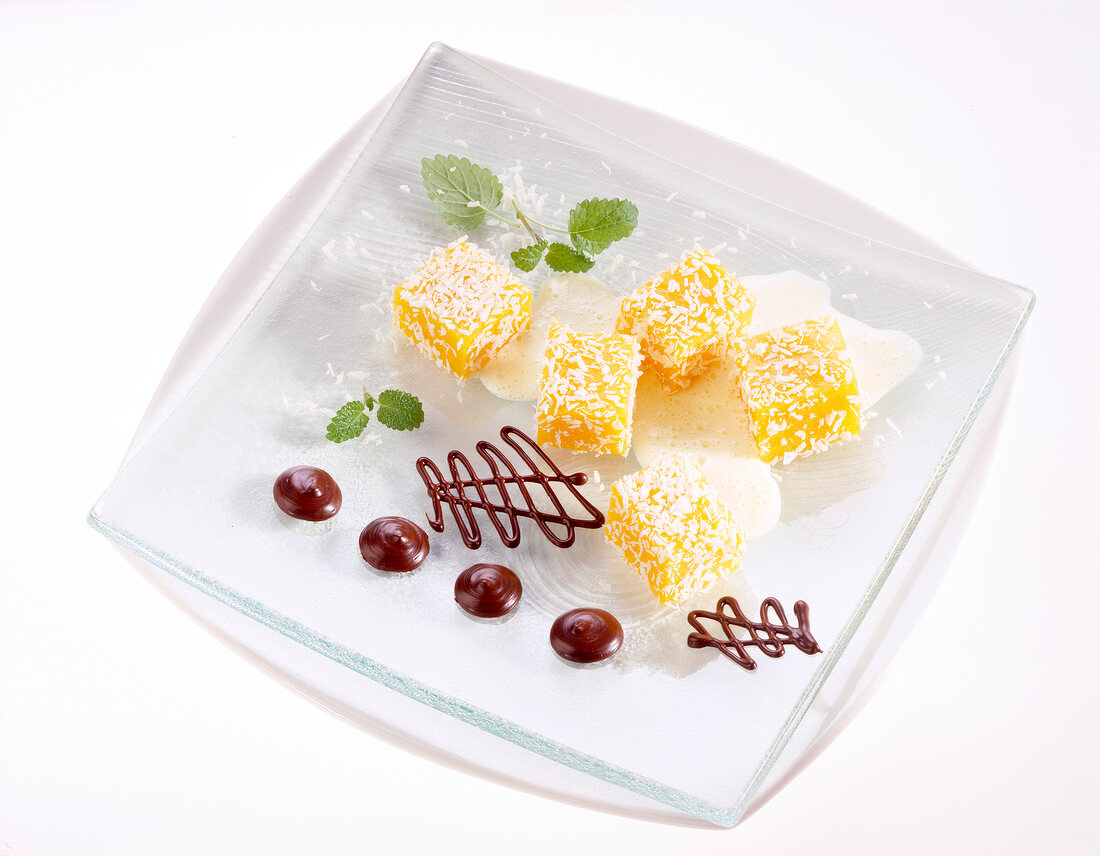 Fruit jelly cubes garnished with grated coconut and chocolate ornaments on glass plate
