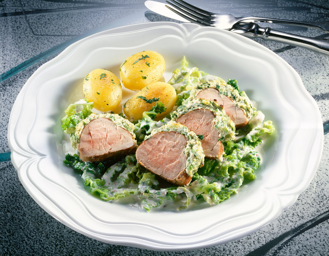 Pork fillet with herb crust, roast potatoes and vegetables on plate