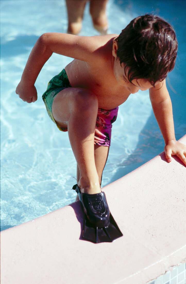 Little boy wearing flippers stepping out of swimming pool