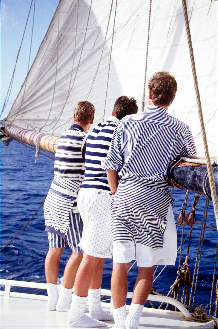 Drei Männer in Sport-Outfit mit Streifenmuster auf einem Segelboot