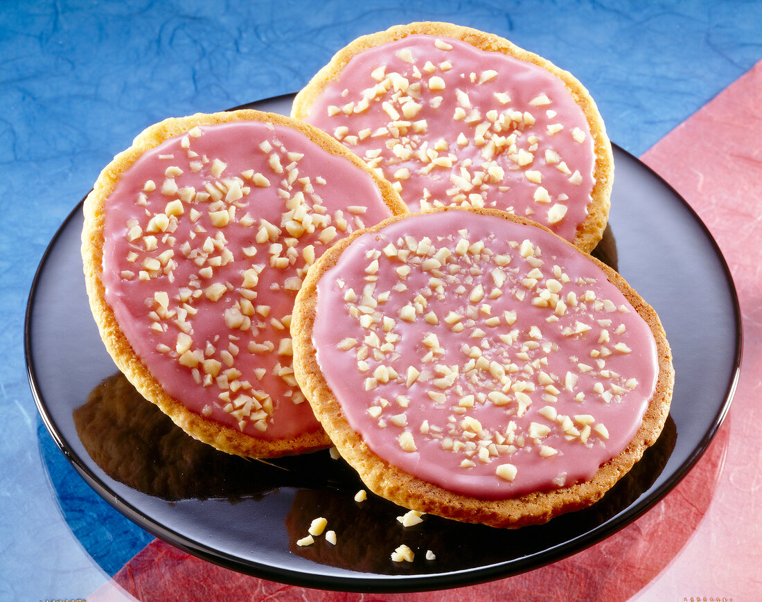 Three American pies with raspberry icing and chopped almonds on plate