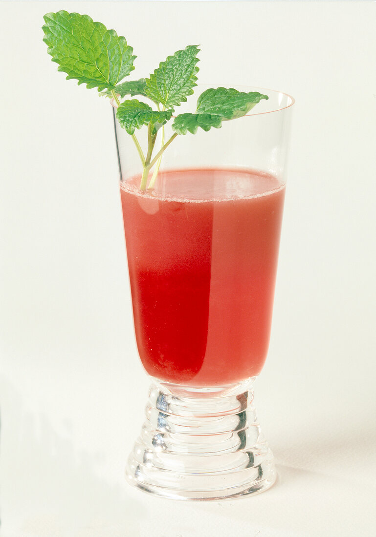 Himbeerdrink im Glas, rot, mit Zitronenmelisseblättchen garniert