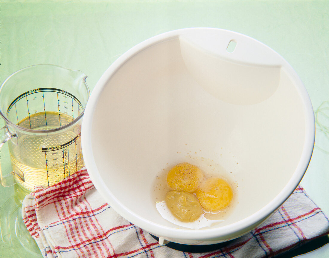 Eggs in bowl beside oil in jar for preparation of mayonnaise