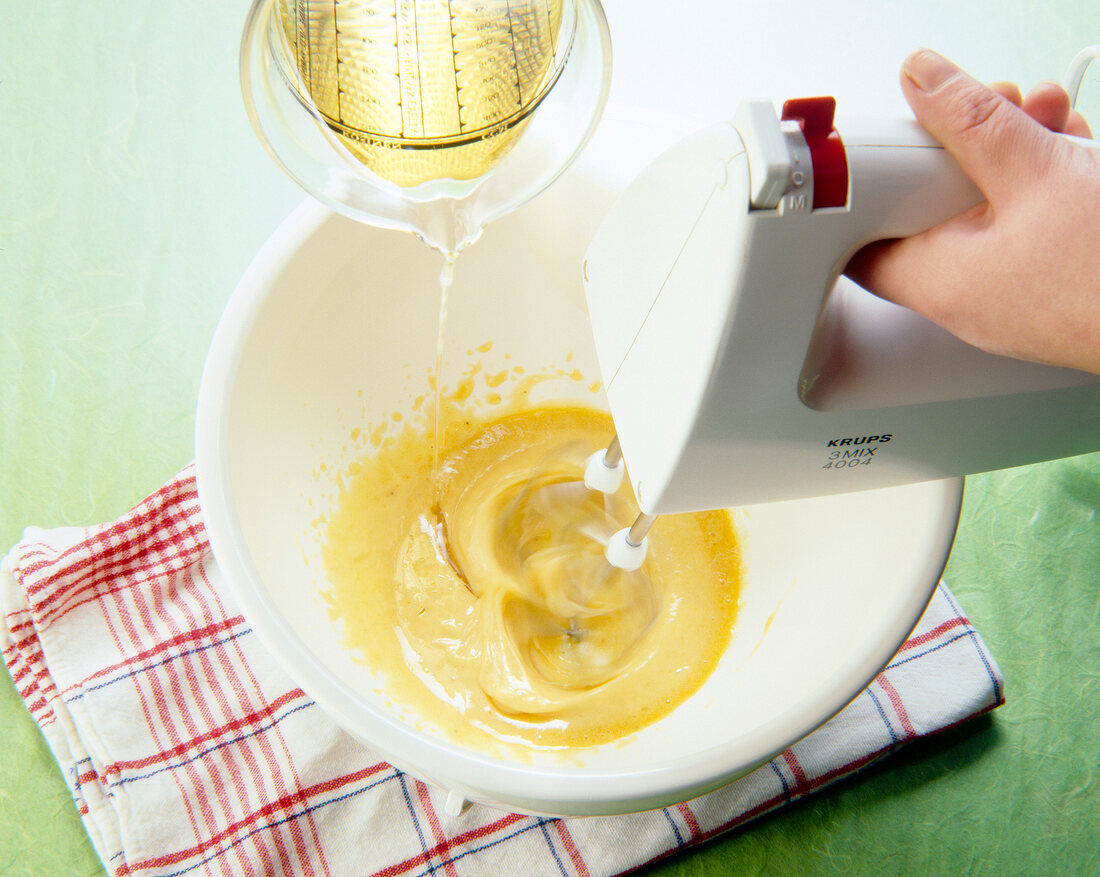 Mixing eggs and oil in bowl with hand whisk for preparation of mayonnaise