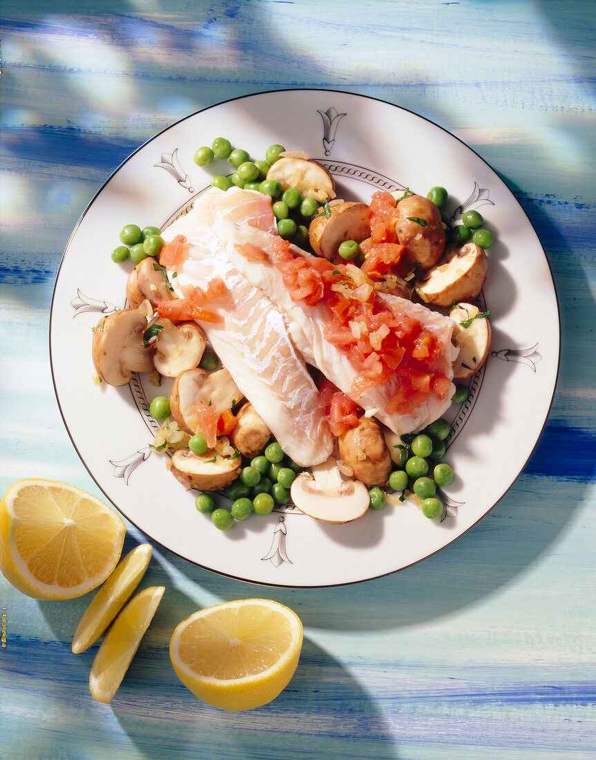 Kabeljaufilet mit Erbsen, Tomaten und Champignons auf Teller