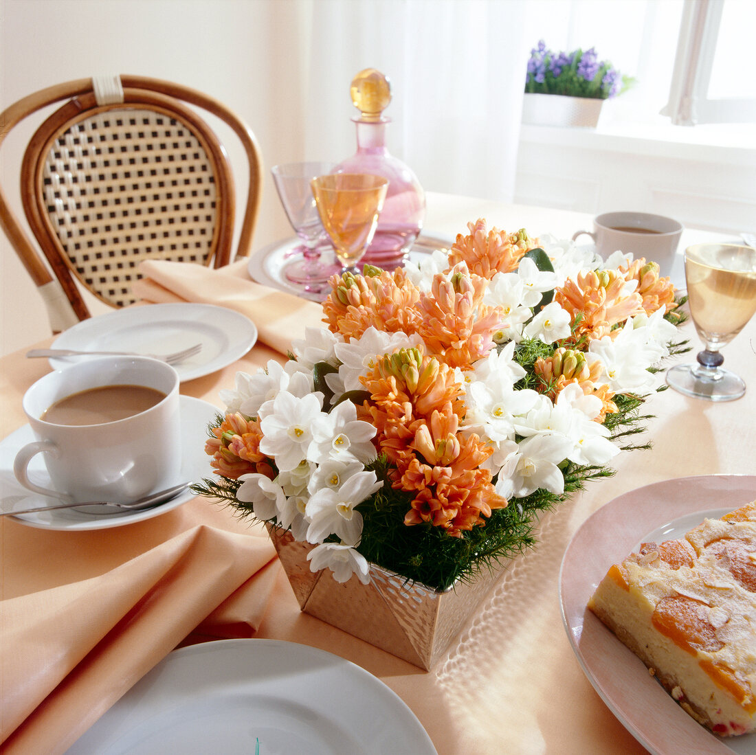 Blumengesteck in einer Backform auf gedecktem Tisch, weiß und orange.
