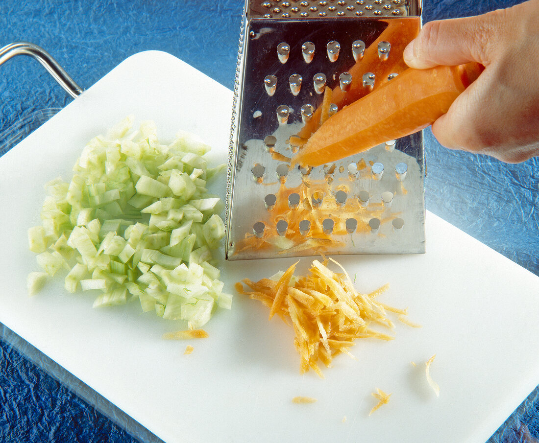 Grating carrots with grater on chopping board