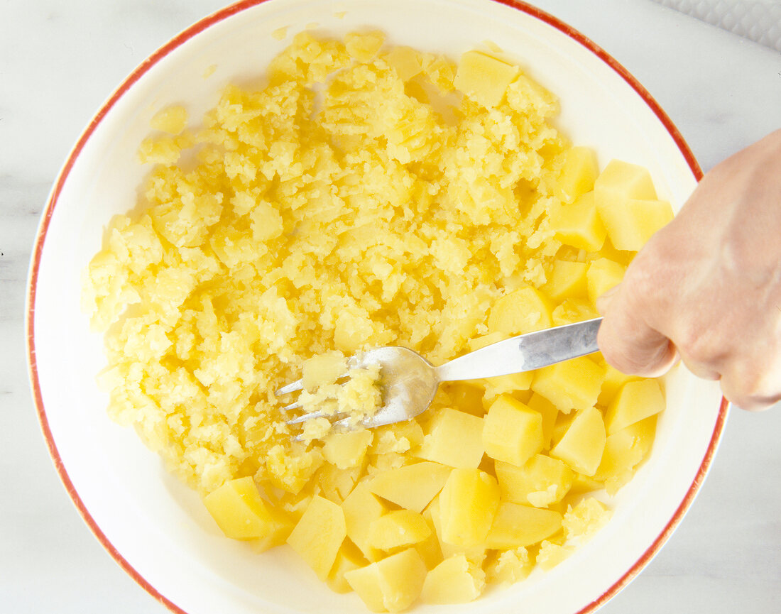 Close-up of diced potatoes being mashed with fork in bowl