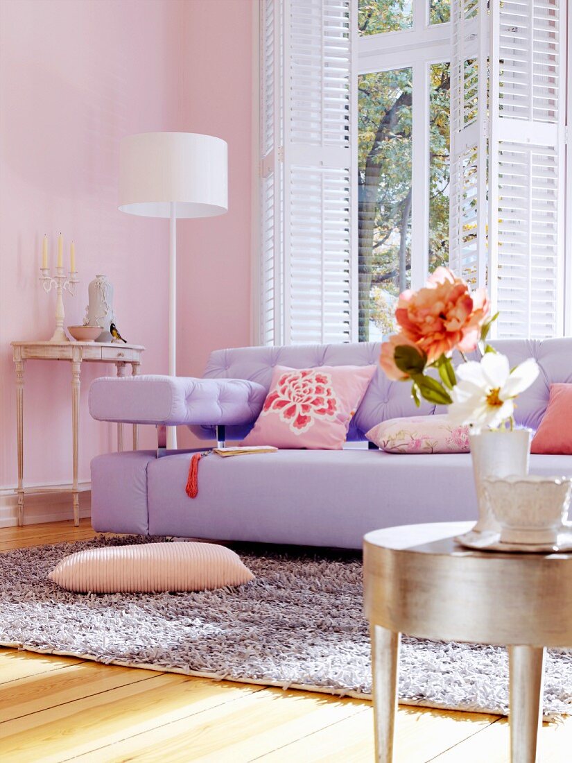Lilac sofa and silver-leaf side table in living room with pink walls