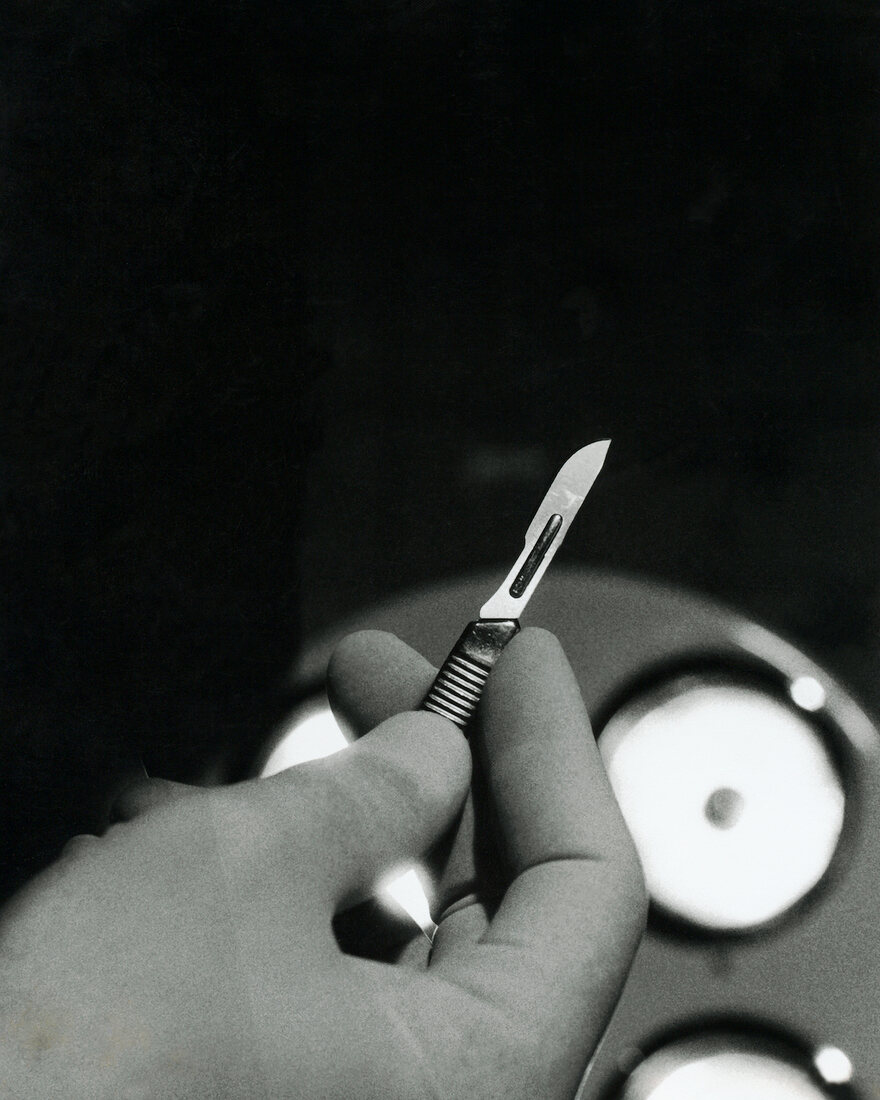 Close-up of surgeon's hand holding scalpel with surgical lights in background 