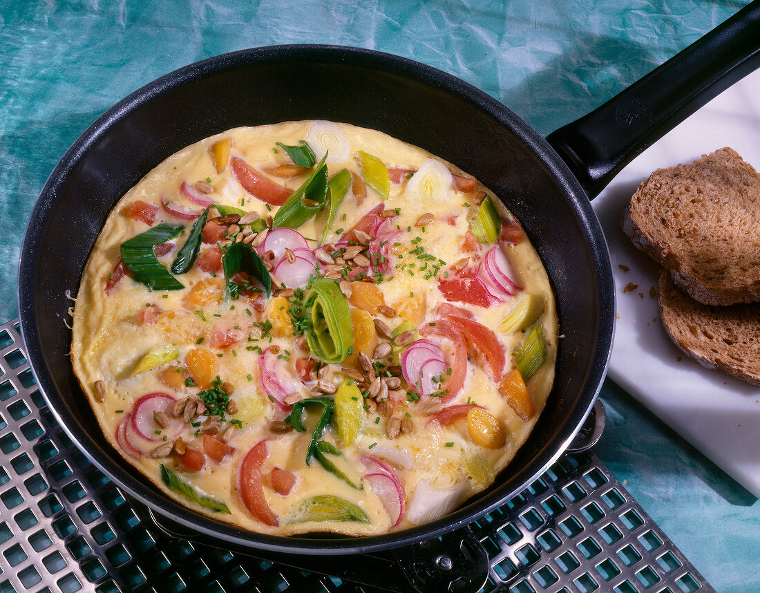 Gemüse-Omelett mit Käse, Radieschen, Porree und Möhren in Pfanne