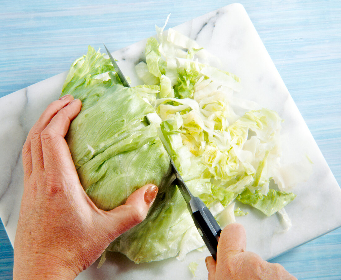 Iceberg lettuce being cut with kitchen knife on chopping board