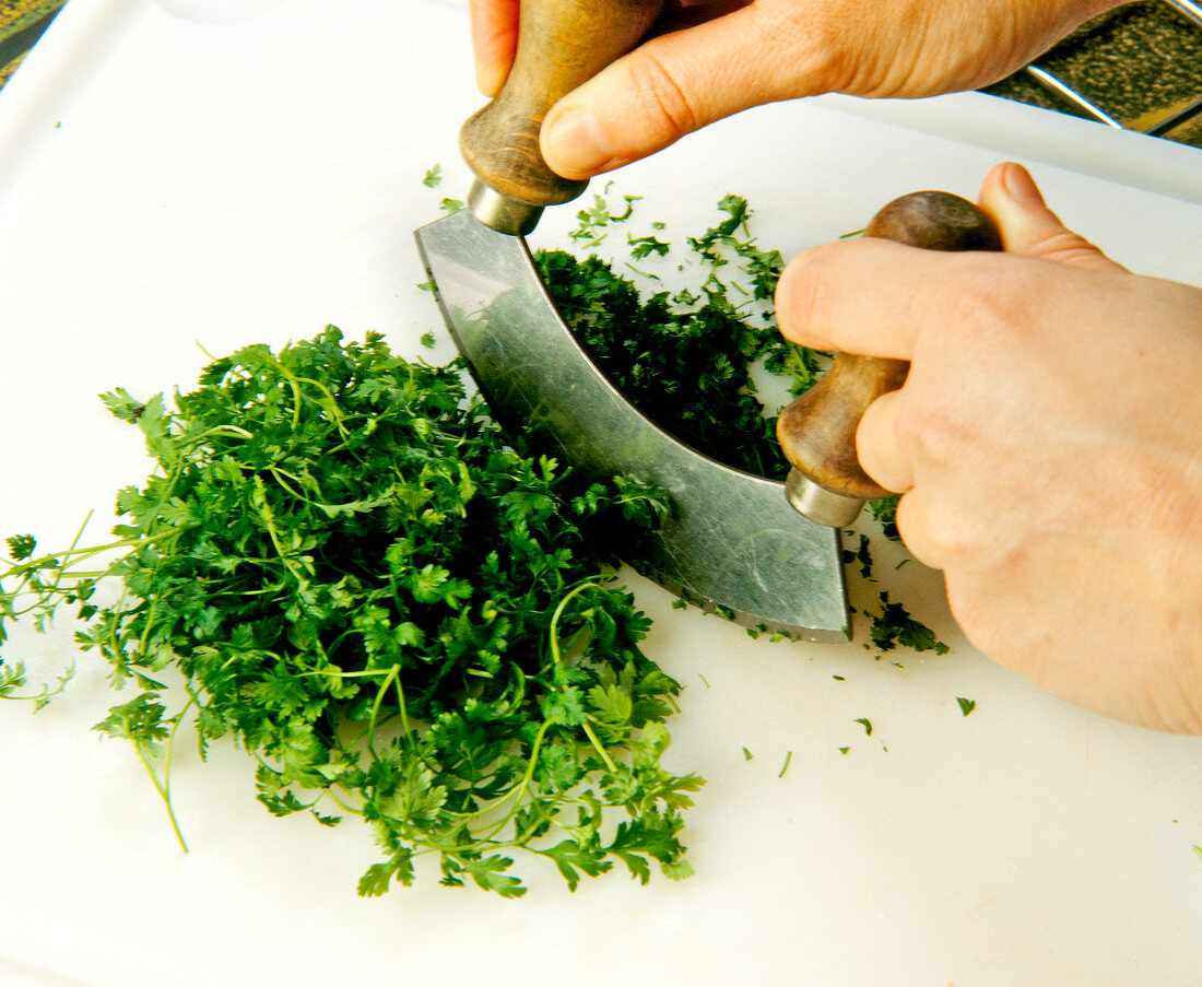 Close-up of parsley being chopped with mezzaluna on tray
