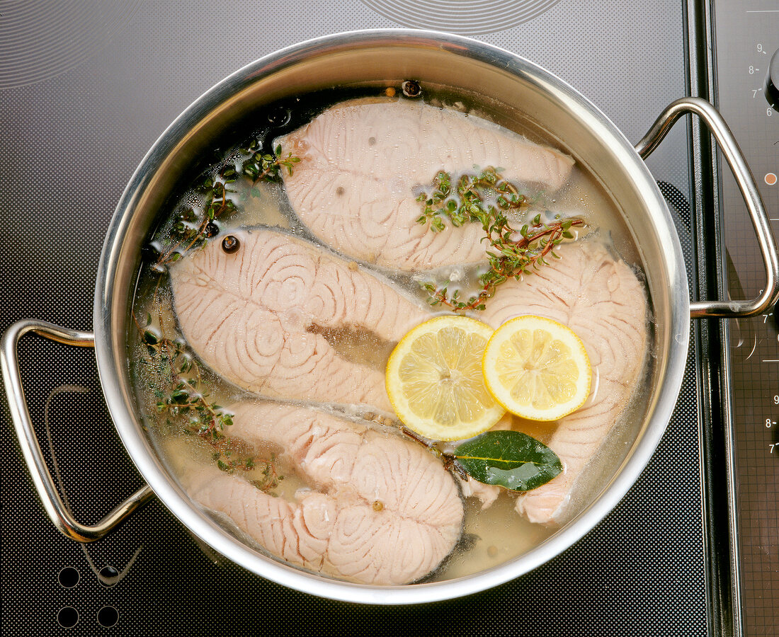Gekochter Fisch, Zitronenscheiben und Gewürze im Kochtopf, close-up.