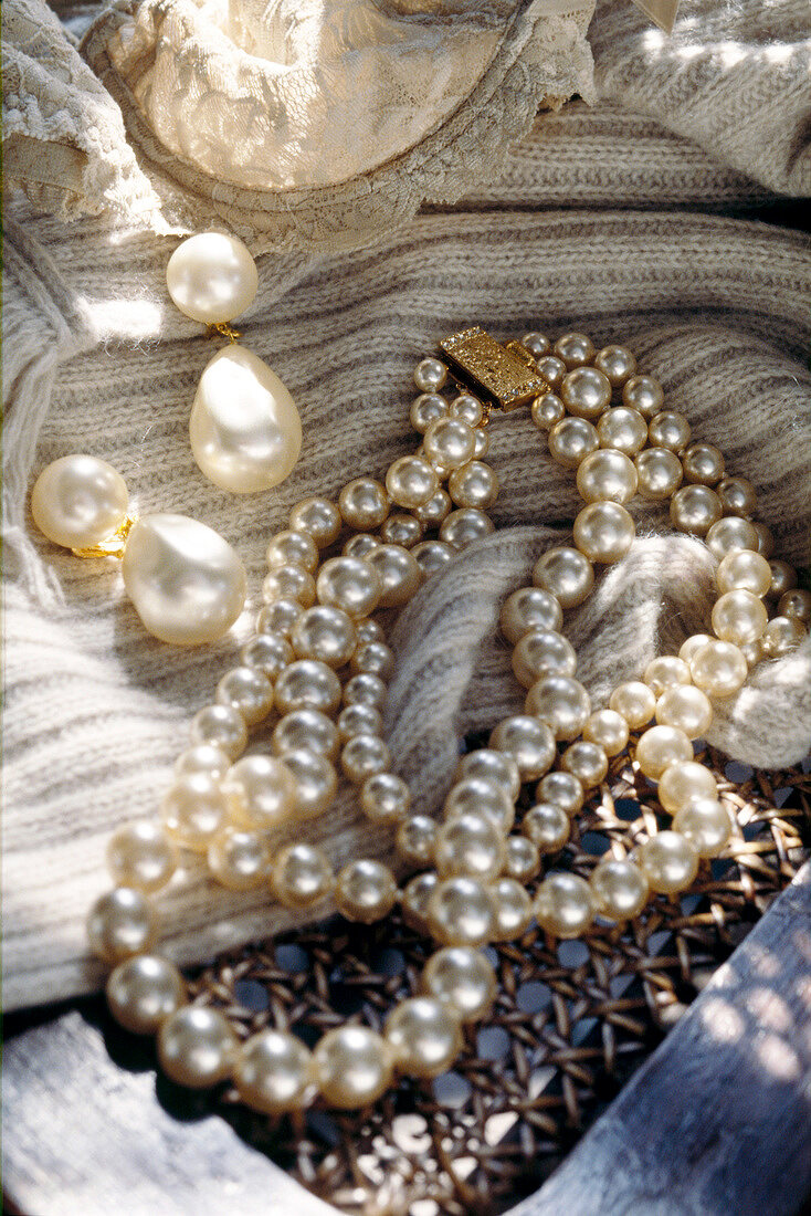 Close-up of various pearl jewellery on knitted scarf