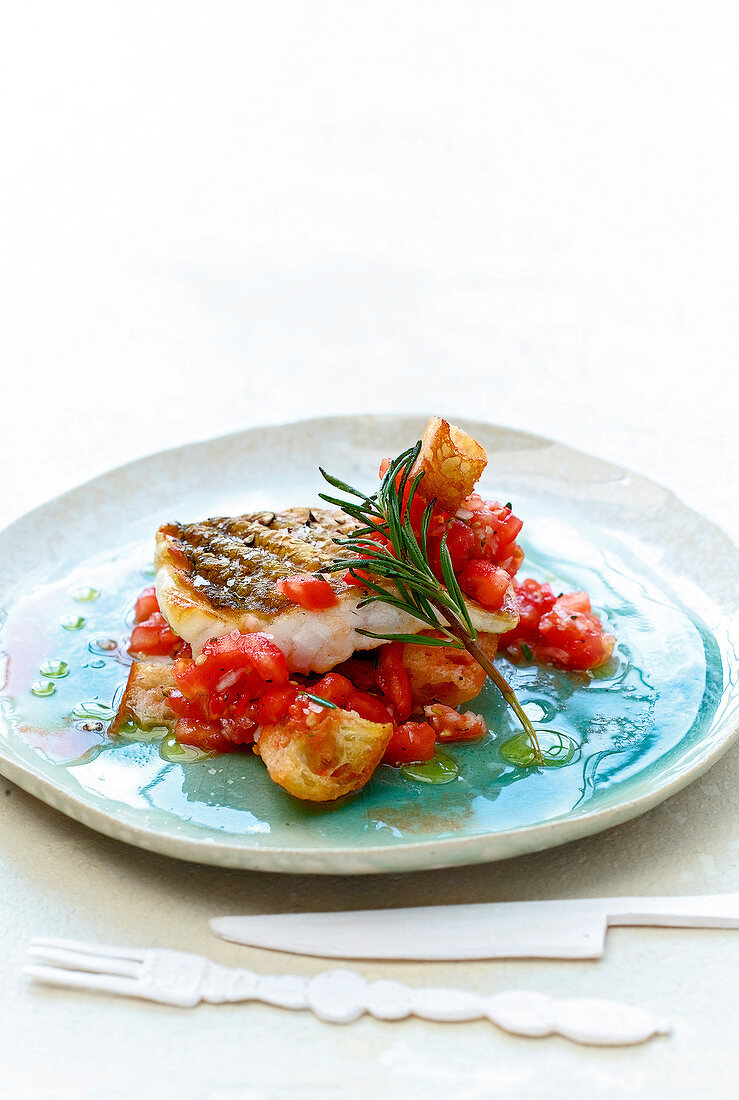 Grilled sea bass with tomato salsa and a sprig of rosemary on plate