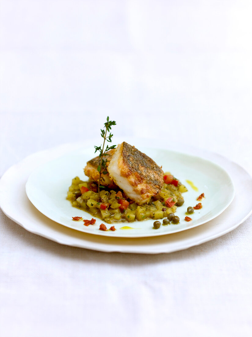 Fried fish with potato risotto, capers and sprig of thyme on plate