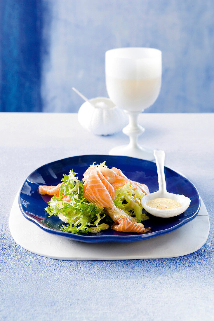 Friséesalat mit Sashimi vom Lachs auf blauem Teller