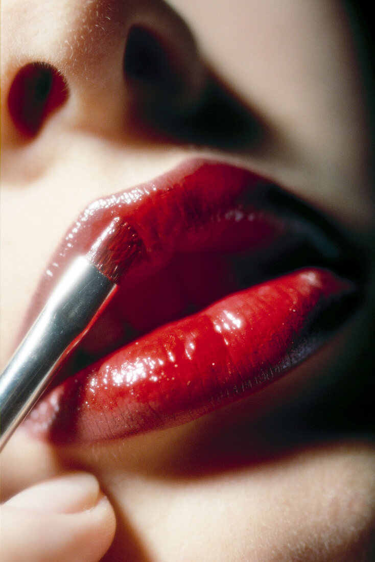 Close-up of woman applying red lipstick on lips