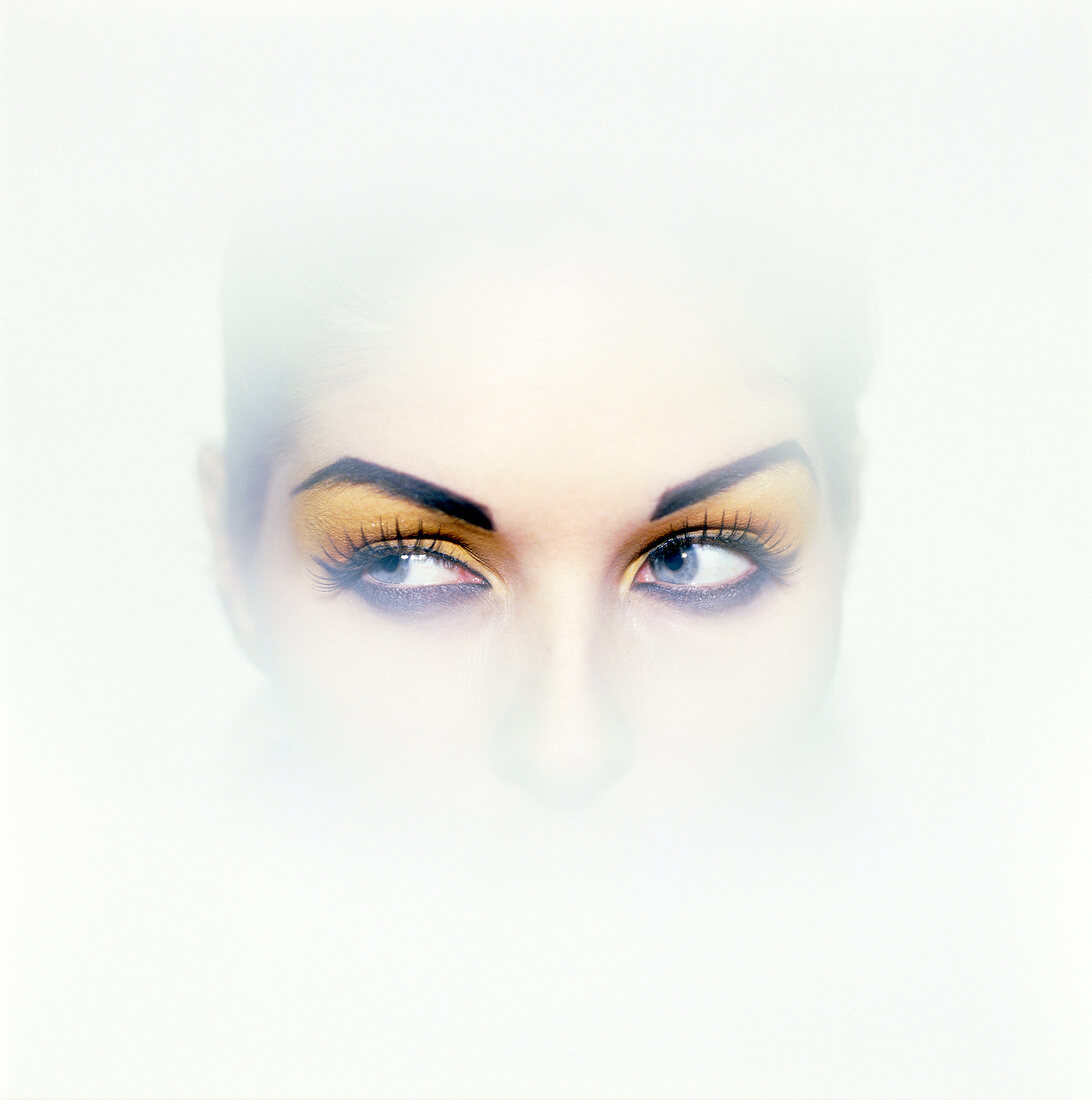 Close-up of woman's thoughtful eyes looking away wearing yellow eye shadow