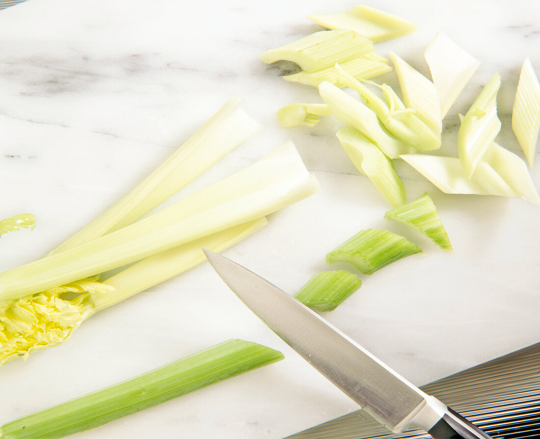 Celery cut obliquely with knife on cutting board