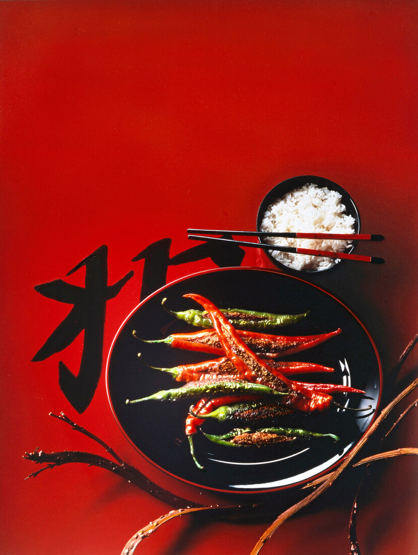 Small bowl of chinese rice with chopsticks and stuffed peppers on plate