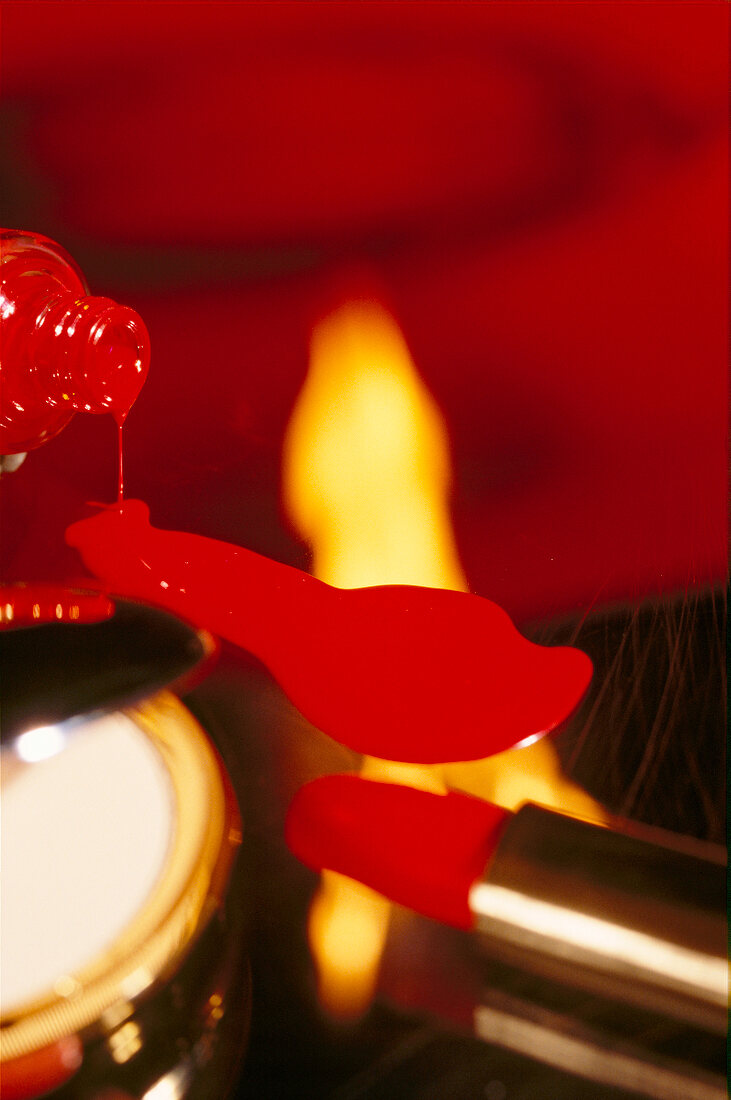 Close-up of red nail polish dripping from bottle, flame and red lipstick