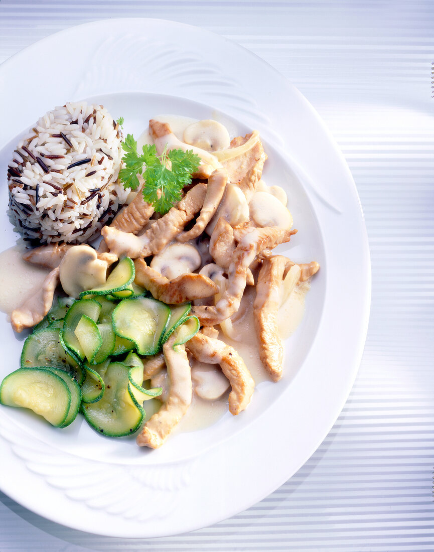 Sliced turkey with wild rice, mushrooms and zucchini on plate