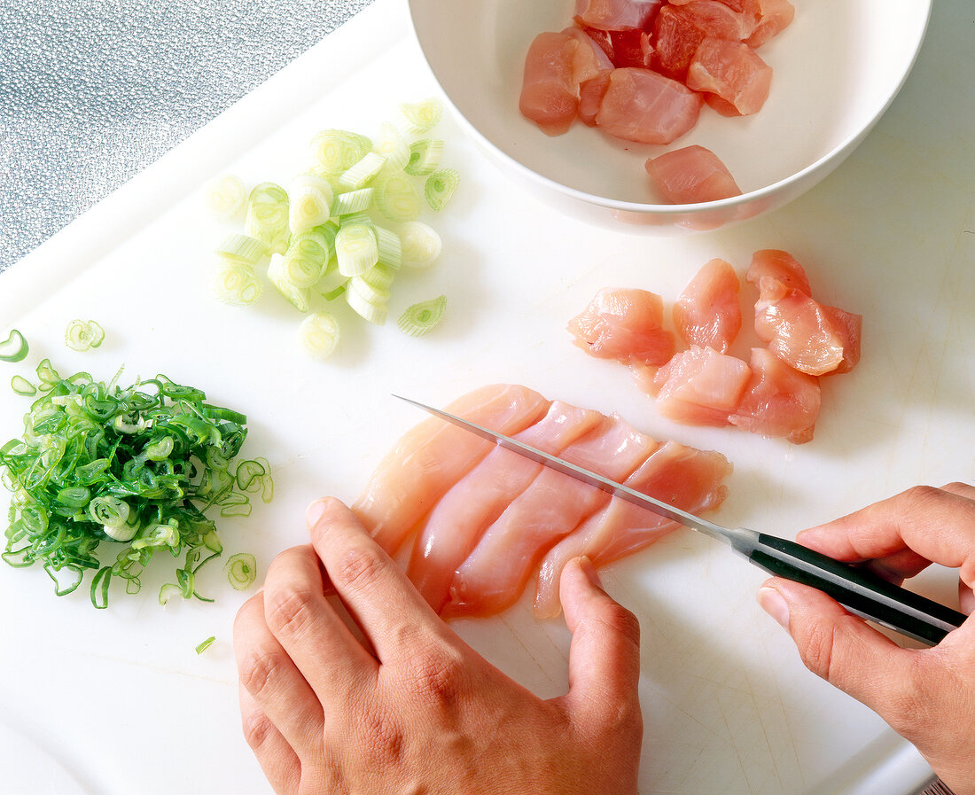 Cutting chicken breast and green onions to small pieces on cutting board