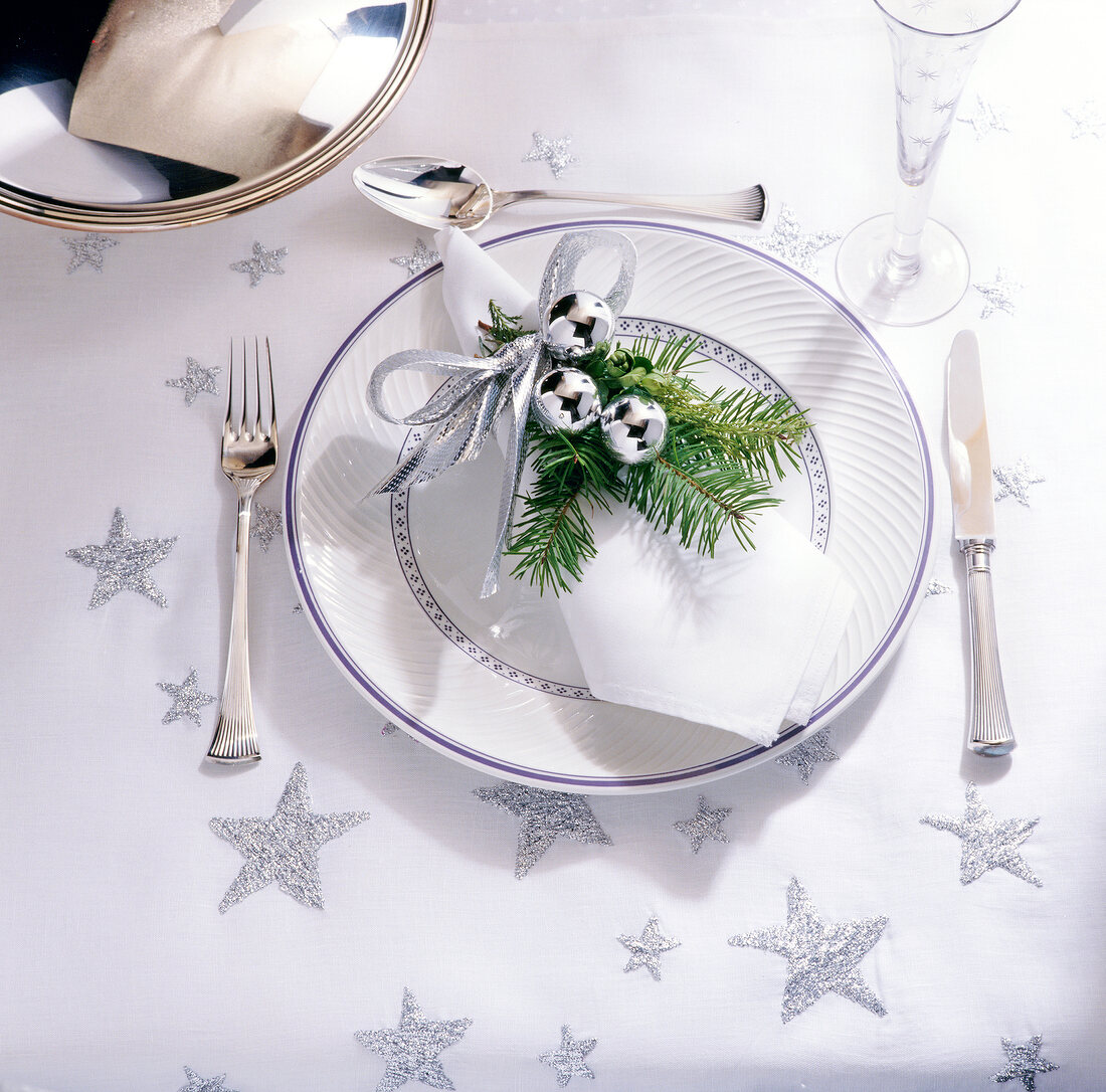 Napkin wrapped with Christmas decoration on plate with knife and fork on table