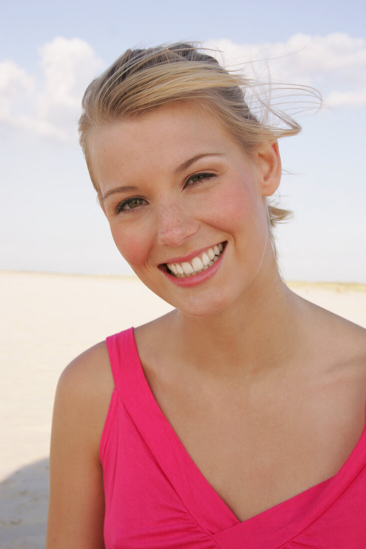 Frau mit blonden Haaren trägt pinkest Top u. lacht, am Strand