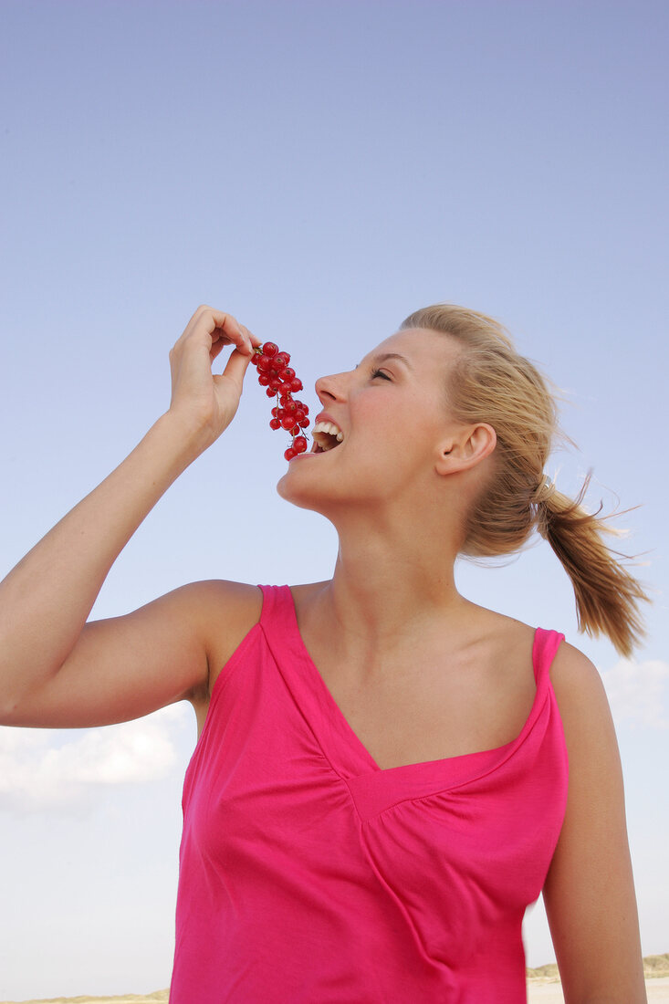 Side view of happy woman holding bunch of red currants near mouth