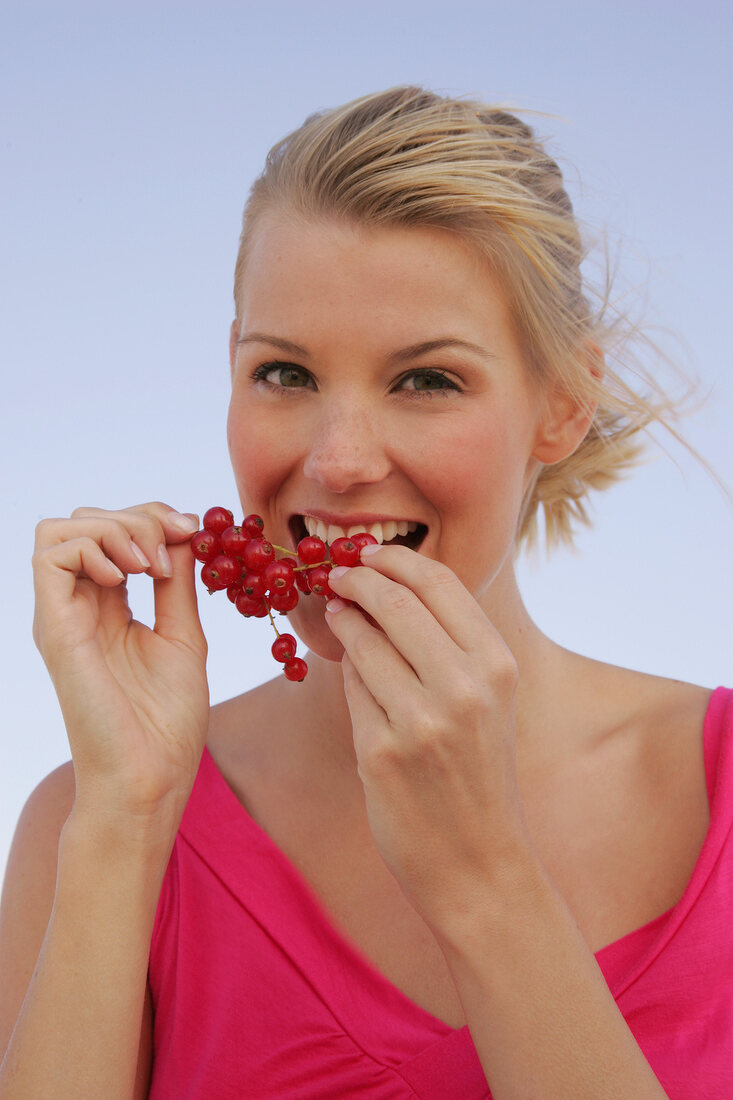 Blonde woman holding a branch of red currants in hand, smiling