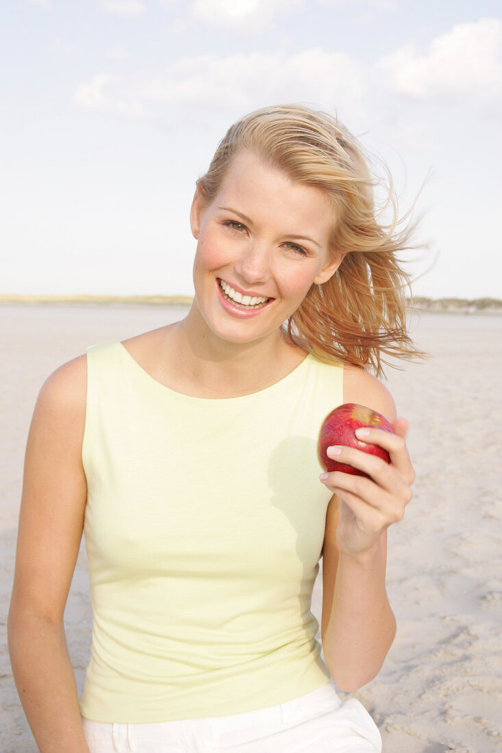 Jennifer Frau am Strand  hält einen Apfel in der Hand, Haare wehen