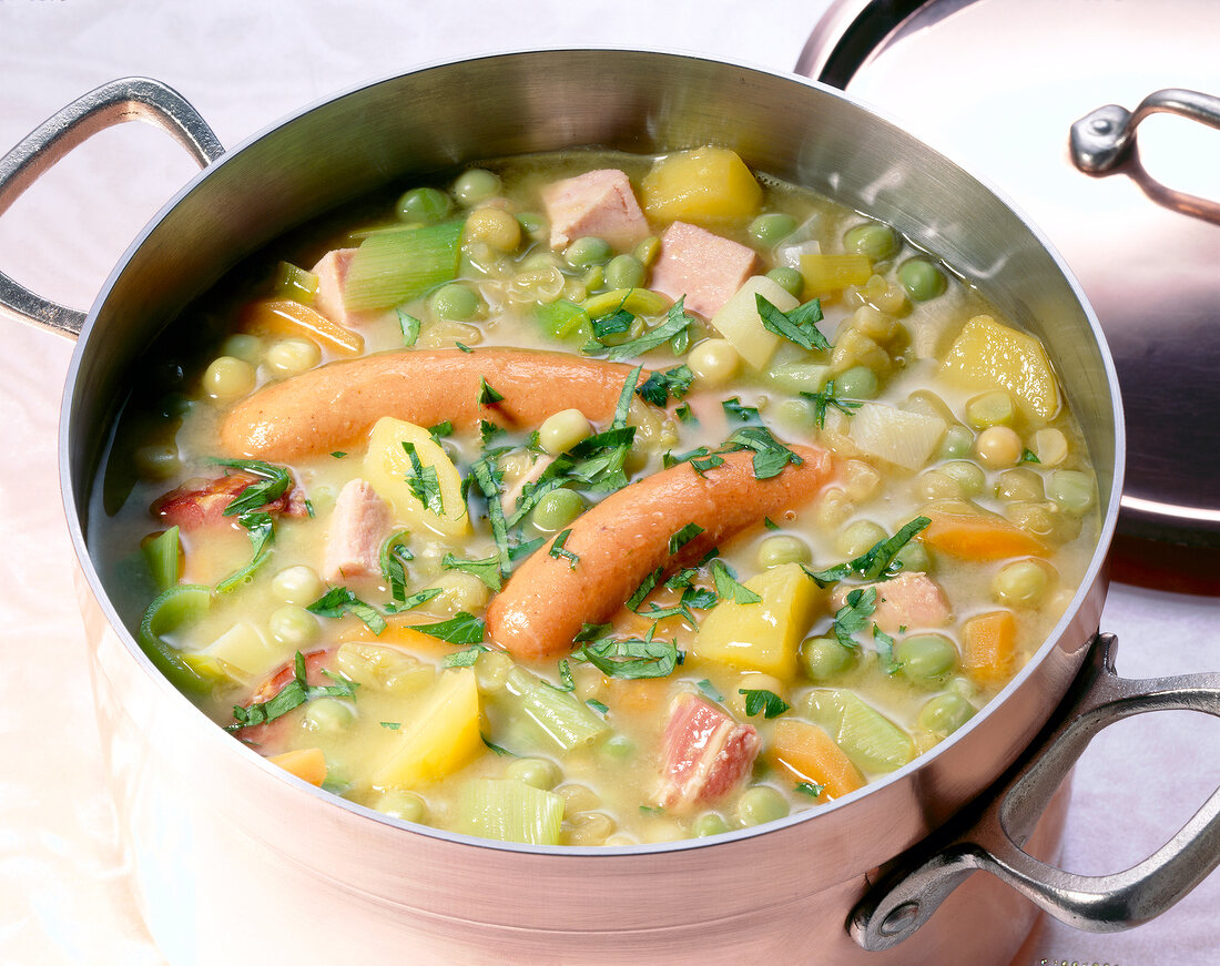 Pea soup with green peas, potatoes and sausages in casserole