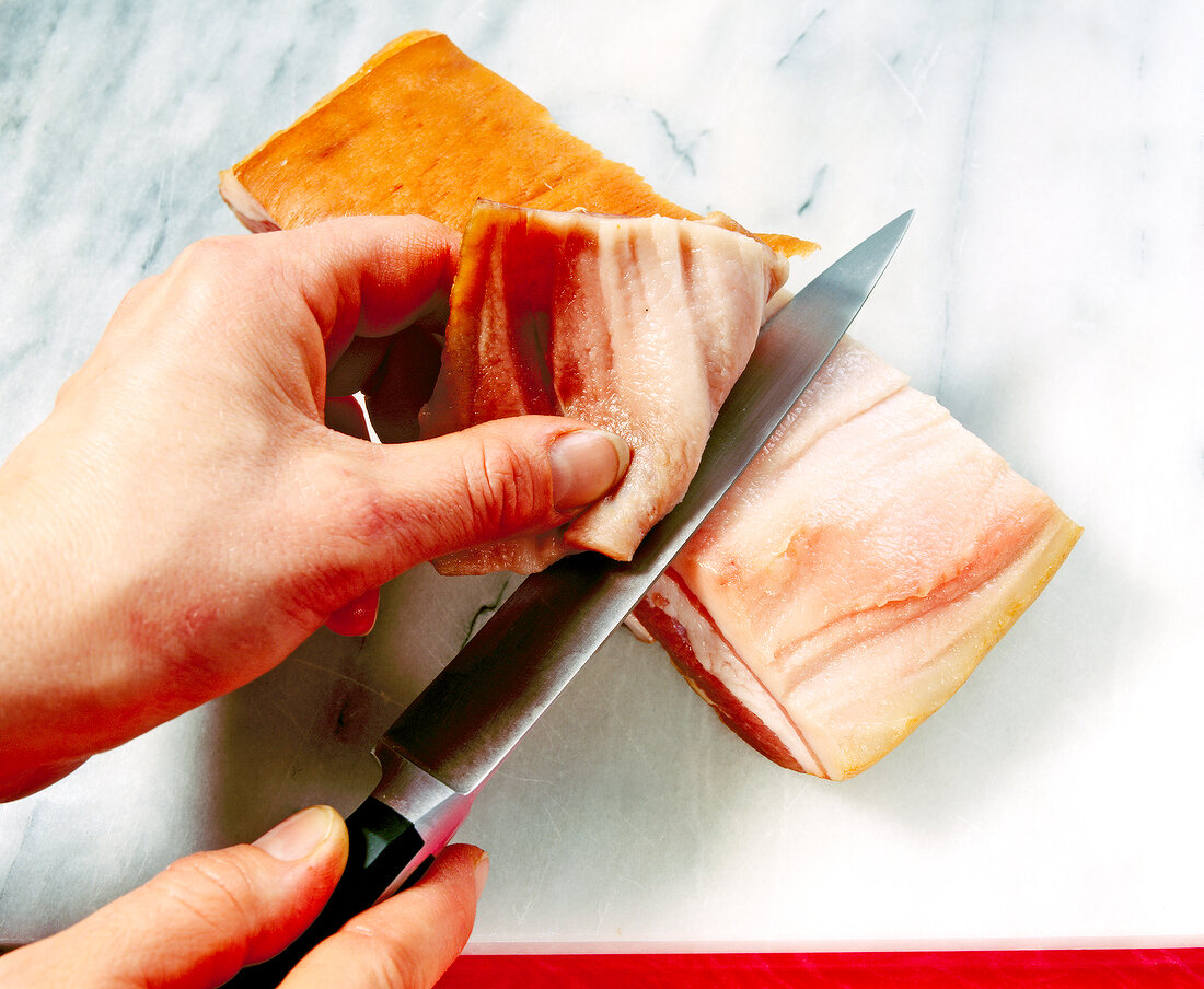 Slicing pork rind off smoked pork with knife